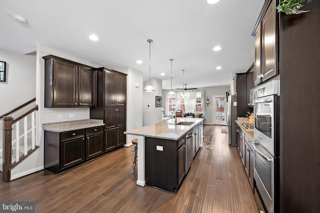 kitchen with decorative light fixtures, a kitchen island with sink, appliances with stainless steel finishes, and dark hardwood / wood-style floors