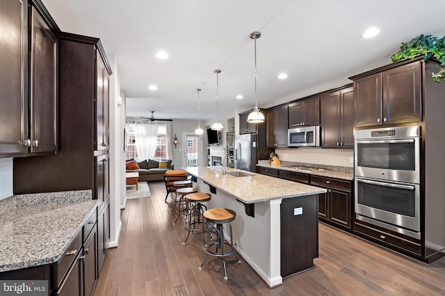 kitchen featuring light stone counters, decorative light fixtures, dark wood-type flooring, appliances with stainless steel finishes, and a kitchen bar