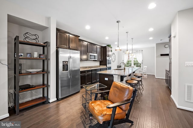 kitchen with a kitchen island with sink, stainless steel appliances, dark wood-type flooring, and a kitchen breakfast bar