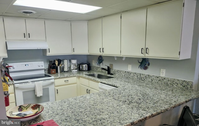 kitchen with light stone counters, kitchen peninsula, sink, white appliances, and a paneled ceiling