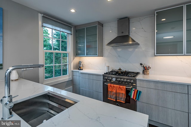 kitchen featuring decorative backsplash, gray cabinets, high end range, sink, and wall chimney range hood