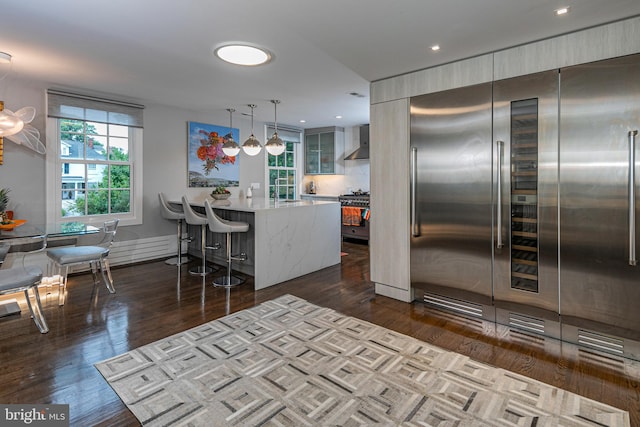 kitchen featuring dark hardwood / wood-style floors, a breakfast bar area, kitchen peninsula, wall chimney exhaust hood, and high quality appliances