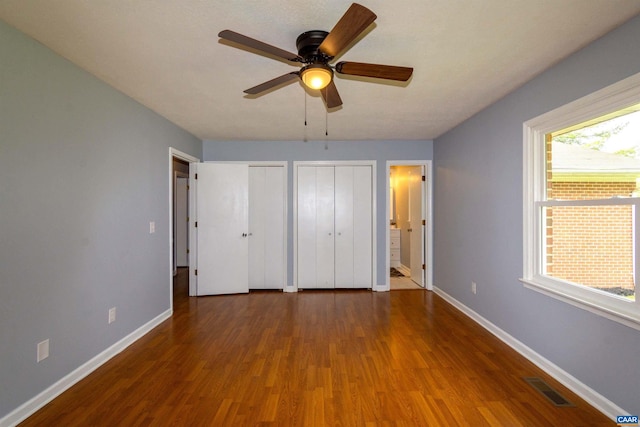 unfurnished bedroom with wood-type flooring, multiple closets, and ceiling fan