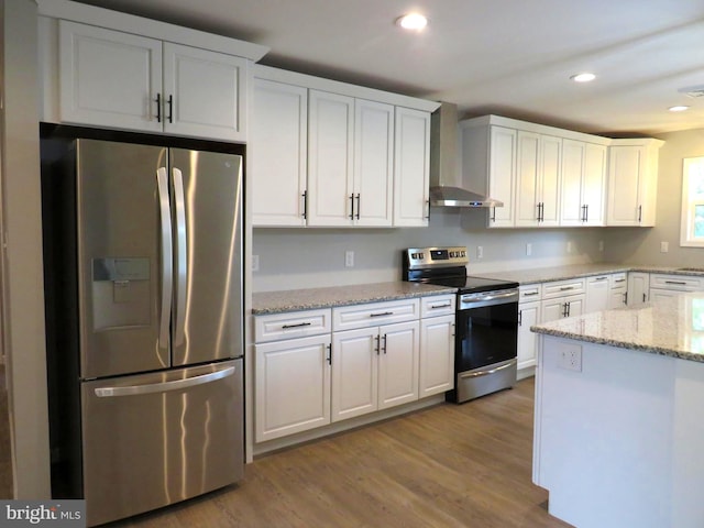 kitchen featuring light stone counters, white cabinets, wall chimney range hood, hardwood / wood-style flooring, and appliances with stainless steel finishes