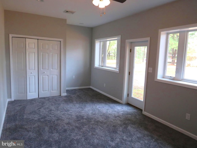 unfurnished bedroom with a closet, dark colored carpet, multiple windows, and ceiling fan