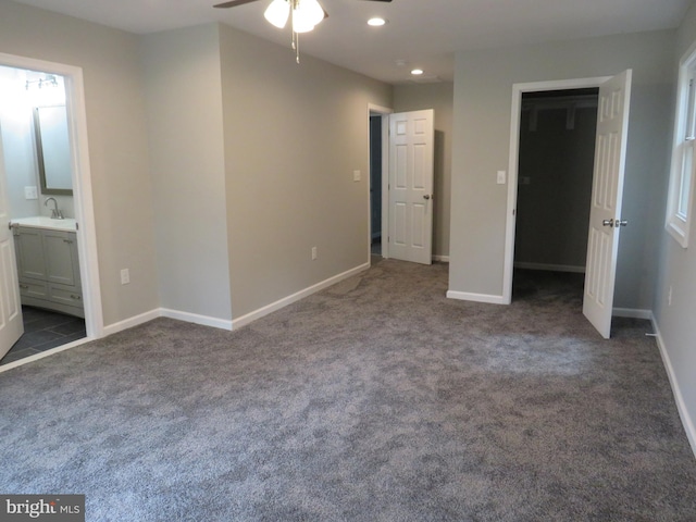 unfurnished bedroom with a spacious closet, dark carpet, ensuite bathroom, and sink