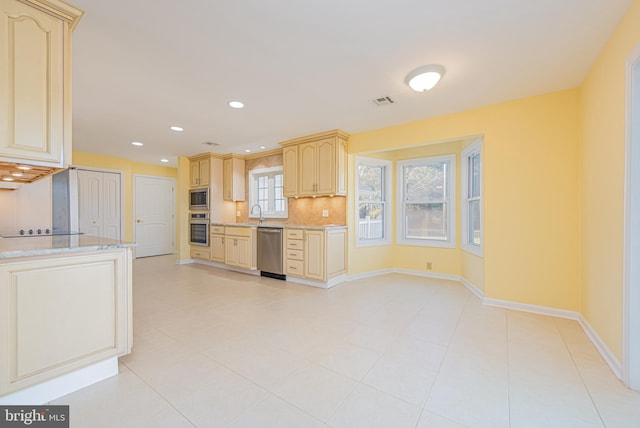 kitchen featuring stainless steel appliances, light stone counters, light tile patterned flooring, backsplash, and light brown cabinets