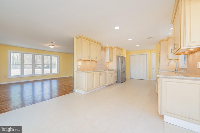 kitchen featuring light hardwood / wood-style floors, light stone counters, sink, tasteful backsplash, and stainless steel fridge with ice dispenser