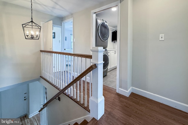 corridor with an inviting chandelier, stacked washer / drying machine, and dark hardwood / wood-style flooring