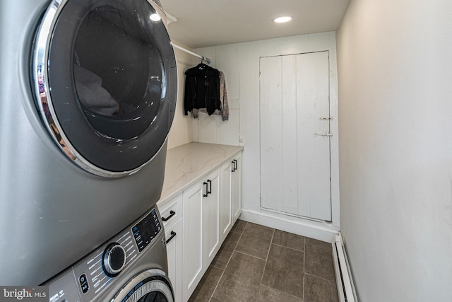 clothes washing area with dark tile patterned floors, stacked washer and clothes dryer, cabinets, and a baseboard heating unit