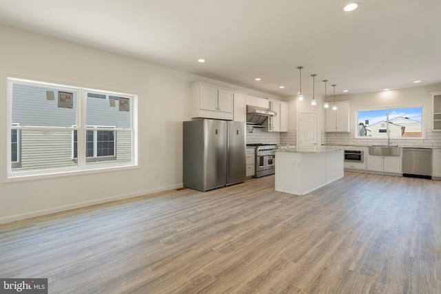 kitchen with white cabinets, decorative light fixtures, ventilation hood, stainless steel appliances, and a center island