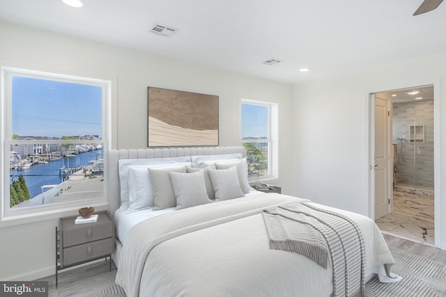 bedroom with wood-type flooring, a water view, and ensuite bath