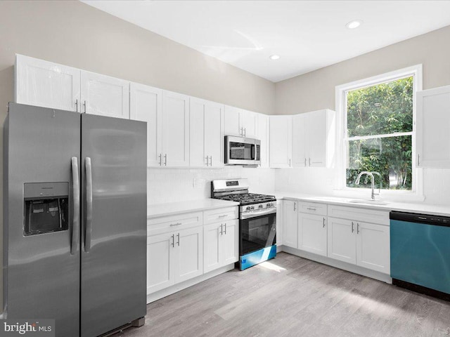 kitchen featuring tasteful backsplash, sink, white cabinetry, light hardwood / wood-style flooring, and appliances with stainless steel finishes