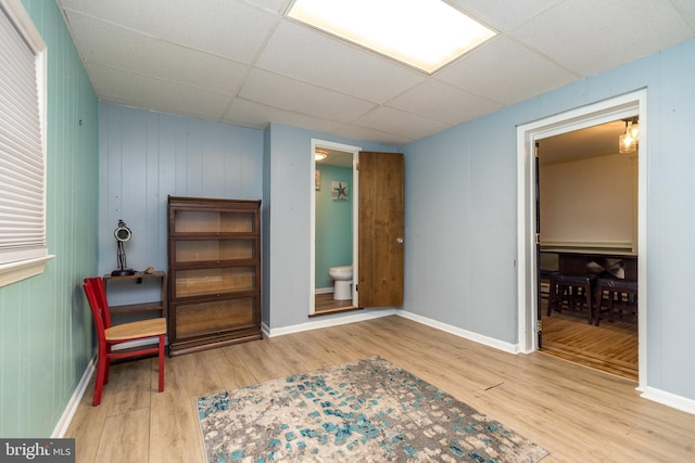 interior space featuring light hardwood / wood-style floors, wood walls, and a drop ceiling