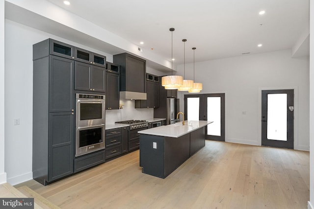 kitchen with hanging light fixtures, sink, a kitchen island with sink, light hardwood / wood-style flooring, and appliances with stainless steel finishes