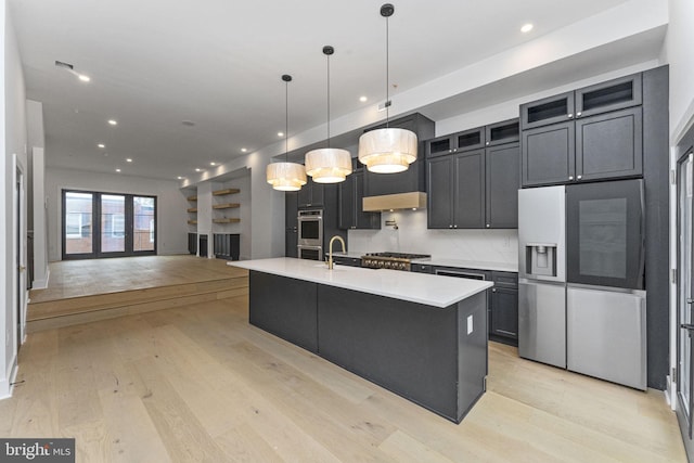 kitchen featuring light wood-type flooring, a center island with sink, appliances with stainless steel finishes, and decorative light fixtures