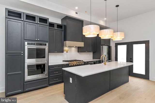 kitchen with an island with sink, stainless steel appliances, light hardwood / wood-style floors, and pendant lighting