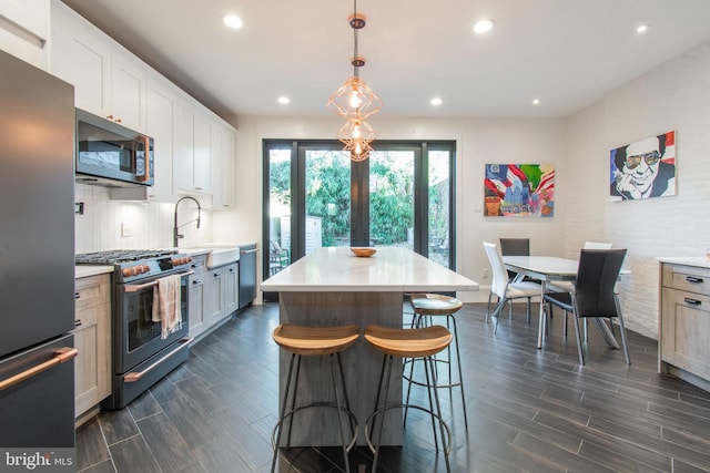 kitchen with a center island, white cabinets, appliances with stainless steel finishes, decorative light fixtures, and dark hardwood / wood-style flooring