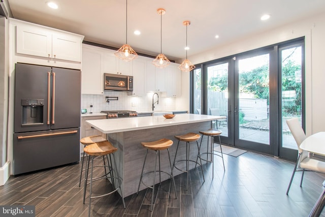 kitchen with hanging light fixtures, white cabinetry, dark wood-type flooring, stainless steel appliances, and a center island