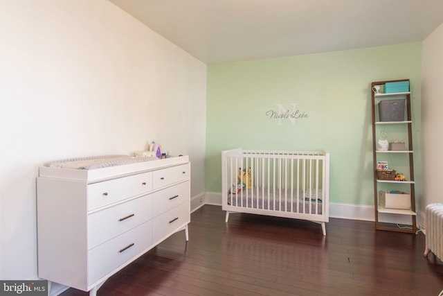 bedroom featuring a nursery area and dark hardwood / wood-style floors