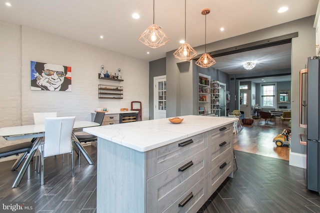 kitchen with light stone counters, stainless steel refrigerator, a kitchen island, pendant lighting, and dark hardwood / wood-style floors