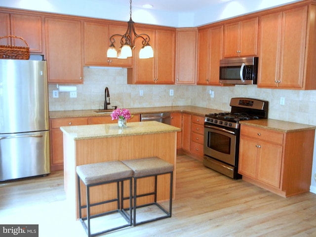 kitchen featuring appliances with stainless steel finishes, hanging light fixtures, a kitchen island, light hardwood / wood-style flooring, and a notable chandelier