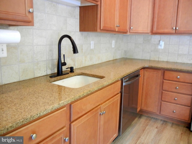 kitchen with light hardwood / wood-style floors, tasteful backsplash, light stone countertops, dishwasher, and sink