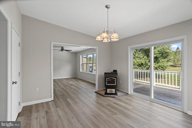 interior space featuring ceiling fan with notable chandelier, a wood stove, lofted ceiling, and light hardwood / wood-style floors