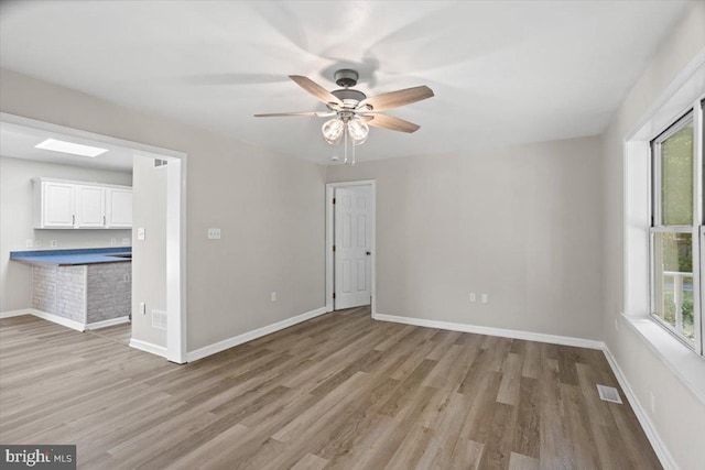 unfurnished room featuring ceiling fan, a skylight, plenty of natural light, and light hardwood / wood-style floors