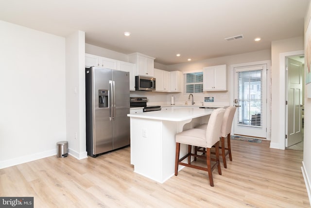 kitchen featuring a kitchen island, light wood-type flooring, stainless steel appliances, white cabinets, and a kitchen breakfast bar