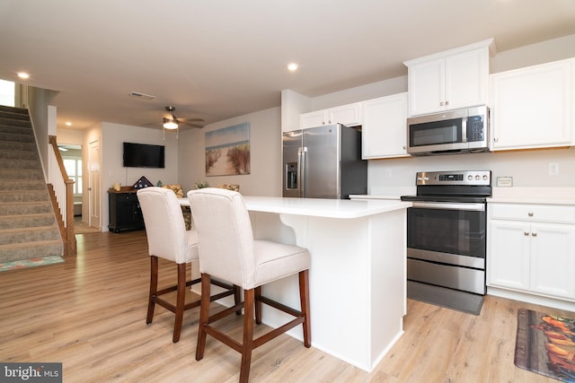 kitchen with a kitchen island, stainless steel appliances, white cabinets, light hardwood / wood-style flooring, and a kitchen bar