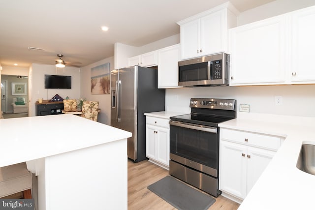 kitchen with ceiling fan, light hardwood / wood-style flooring, stainless steel appliances, white cabinets, and a kitchen bar