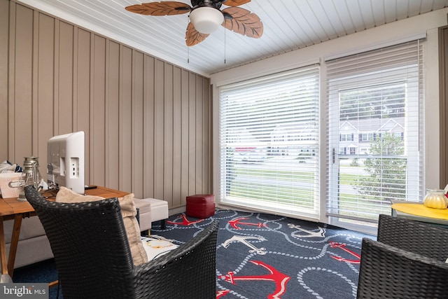 sitting room featuring wood walls, a wealth of natural light, and ceiling fan