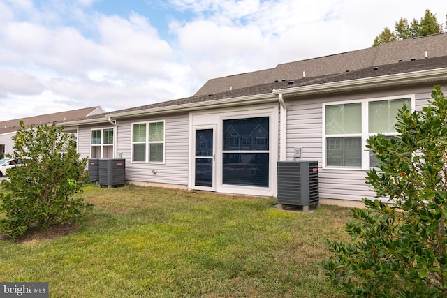 back of property with central AC unit and a yard