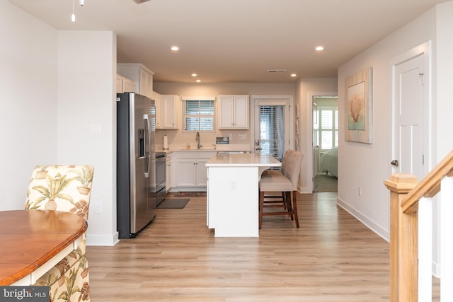 kitchen with a center island, stainless steel appliances, sink, white cabinetry, and light hardwood / wood-style flooring