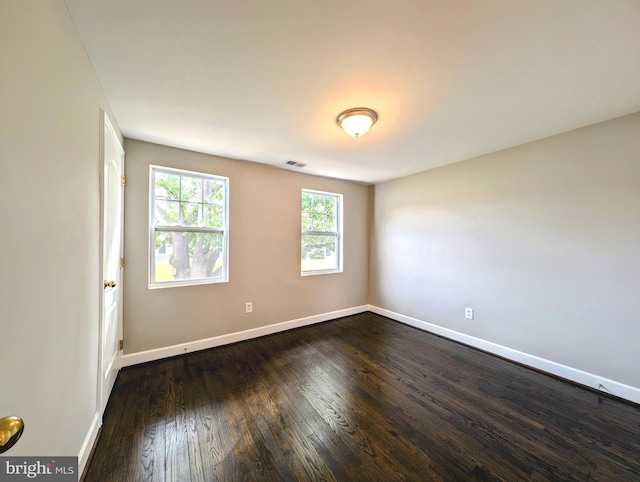 unfurnished room featuring baseboards, visible vents, and dark wood finished floors