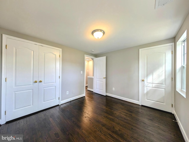 unfurnished bedroom featuring baseboards, visible vents, a closet, and dark wood finished floors