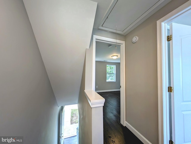 hallway with an upstairs landing, baseboards, attic access, and dark wood finished floors
