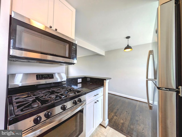 kitchen featuring white cabinets, baseboards, appliances with stainless steel finishes, decorative light fixtures, and light wood-style floors