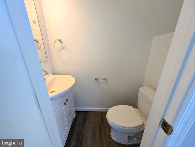 half bathroom with toilet, vanity, baseboards, and wood finished floors