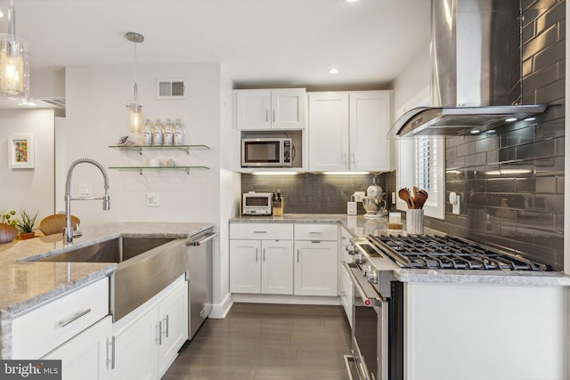 kitchen featuring white cabinets, hanging light fixtures, wall chimney range hood, backsplash, and appliances with stainless steel finishes