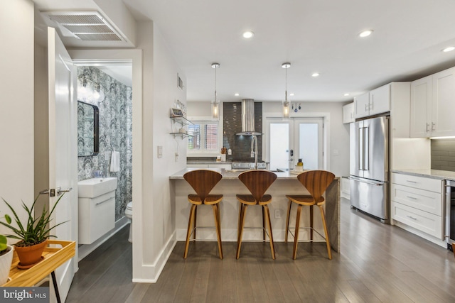 kitchen featuring hanging light fixtures, high end fridge, wall chimney exhaust hood, white cabinetry, and dark hardwood / wood-style floors