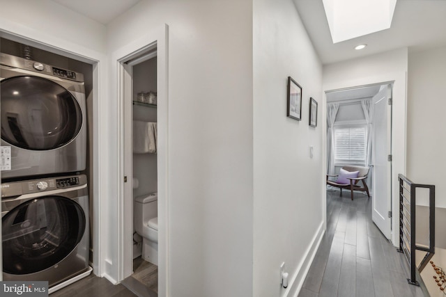 laundry area featuring stacked washer / drying machine, dark hardwood / wood-style floors, and a skylight