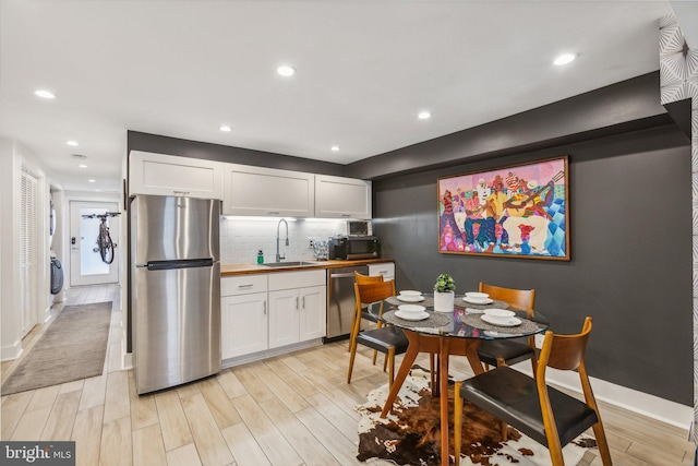 kitchen with light wood-type flooring, tasteful backsplash, sink, white cabinetry, and appliances with stainless steel finishes