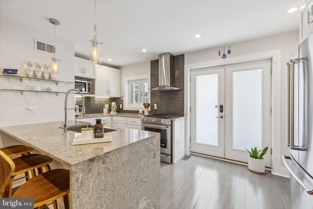 kitchen featuring white cabinetry, kitchen peninsula, wall chimney range hood, a kitchen breakfast bar, and stainless steel appliances