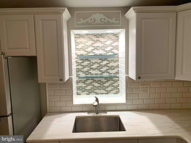 kitchen featuring stainless steel refrigerator, decorative backsplash, sink, and white cabinets