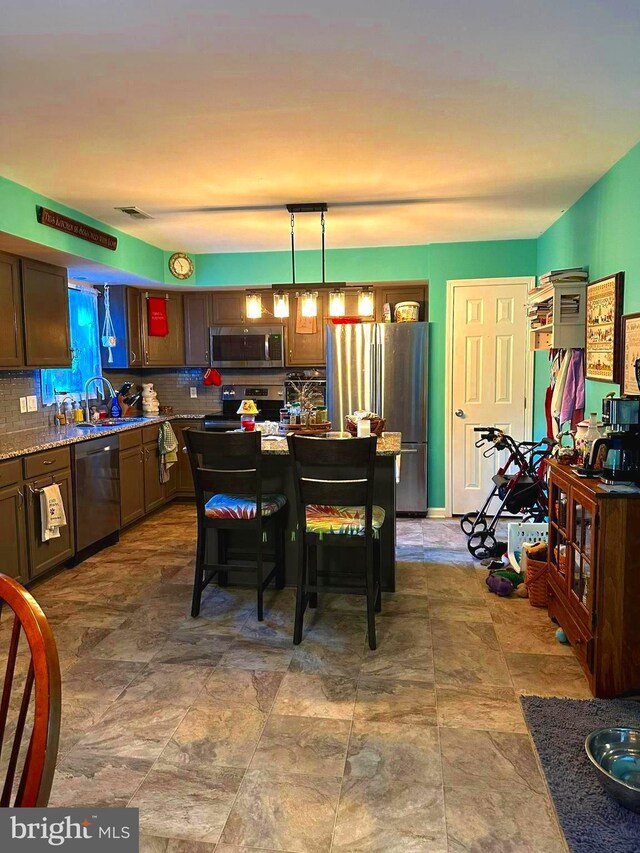 kitchen with pendant lighting, light stone counters, stainless steel appliances, and tasteful backsplash