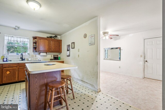 kitchen with a kitchen breakfast bar, ceiling fan, a center island, and sink