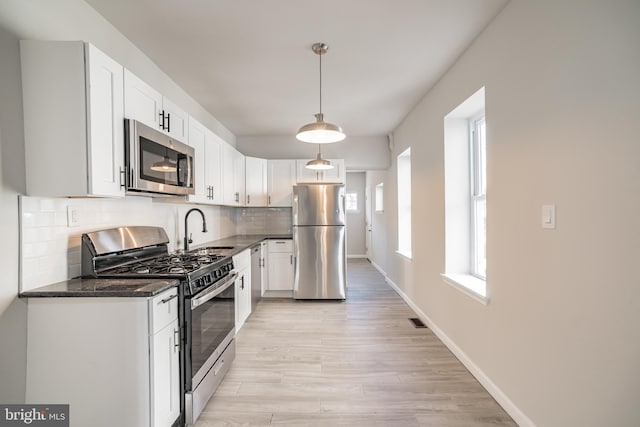 kitchen featuring white cabinets, sink, appliances with stainless steel finishes, light hardwood / wood-style floors, and decorative backsplash