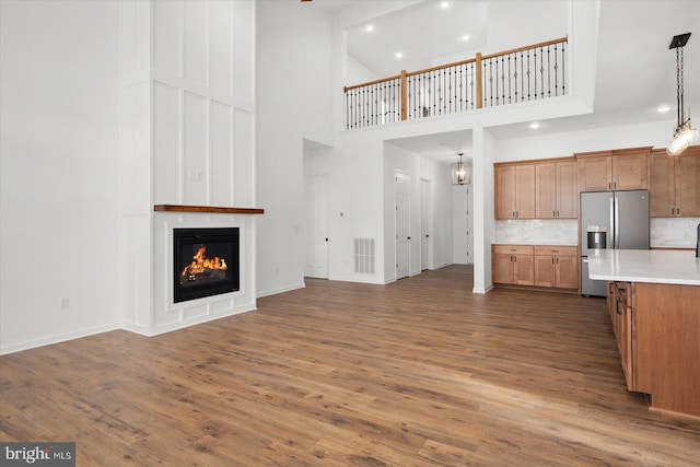 kitchen featuring stainless steel fridge, a towering ceiling, backsplash, dark wood-type flooring, and decorative light fixtures